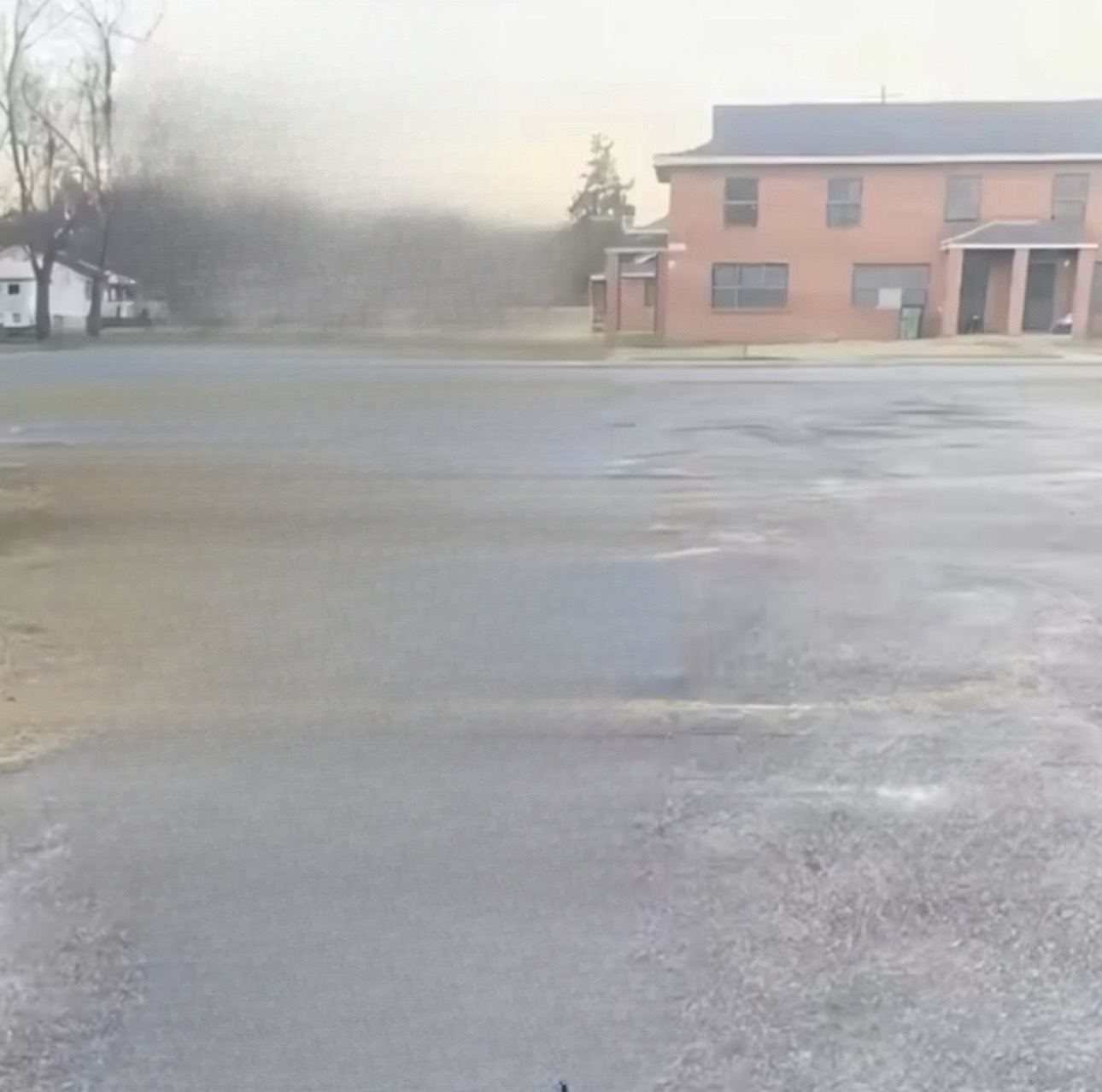 Blank SYBAU meme template - A wet, empty parking lot stretches across the lower two-thirds of the frame. A pink apartment building and some bare trees li