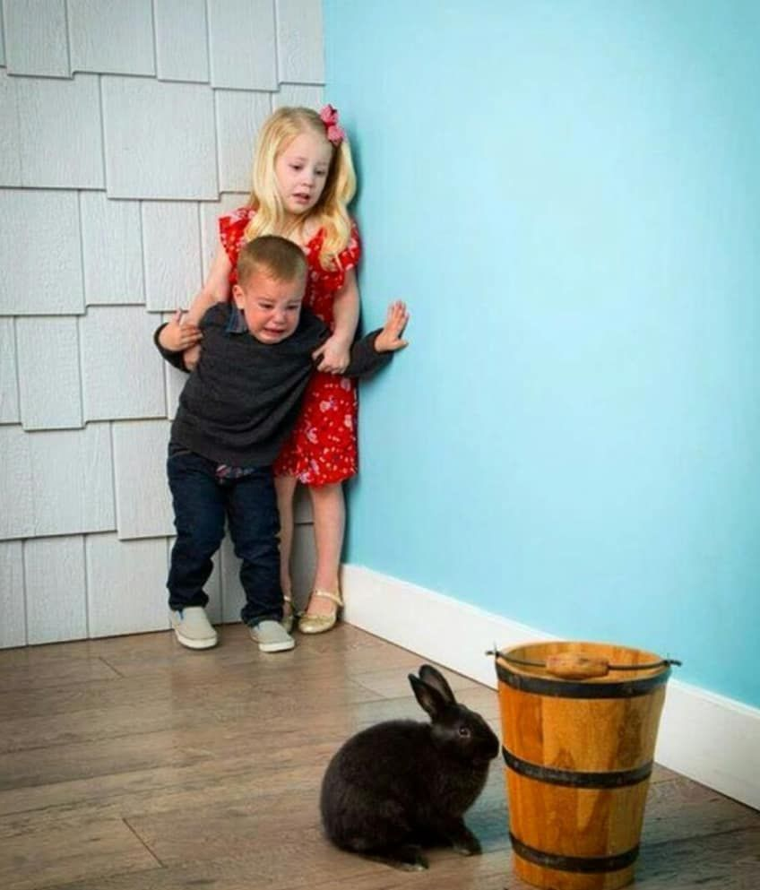 Children Scared Of Rabbit meme template - Two children pressed against a turquoise wall. The girl in red stands behind, gripping the boy's shoulders. The boy in grey l