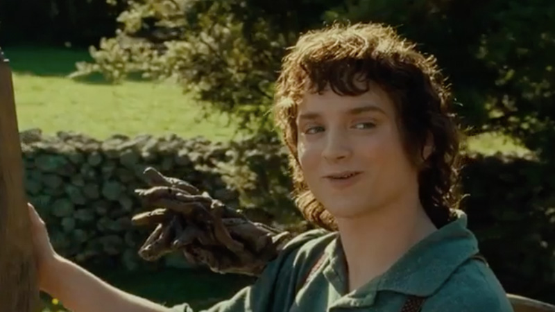 Frodo Keep Your Secrets meme template - Elijah Wood as Frodo Baggins stands in the lush green Shire, one hand resting casually on a wooden fence post, a stone wall a