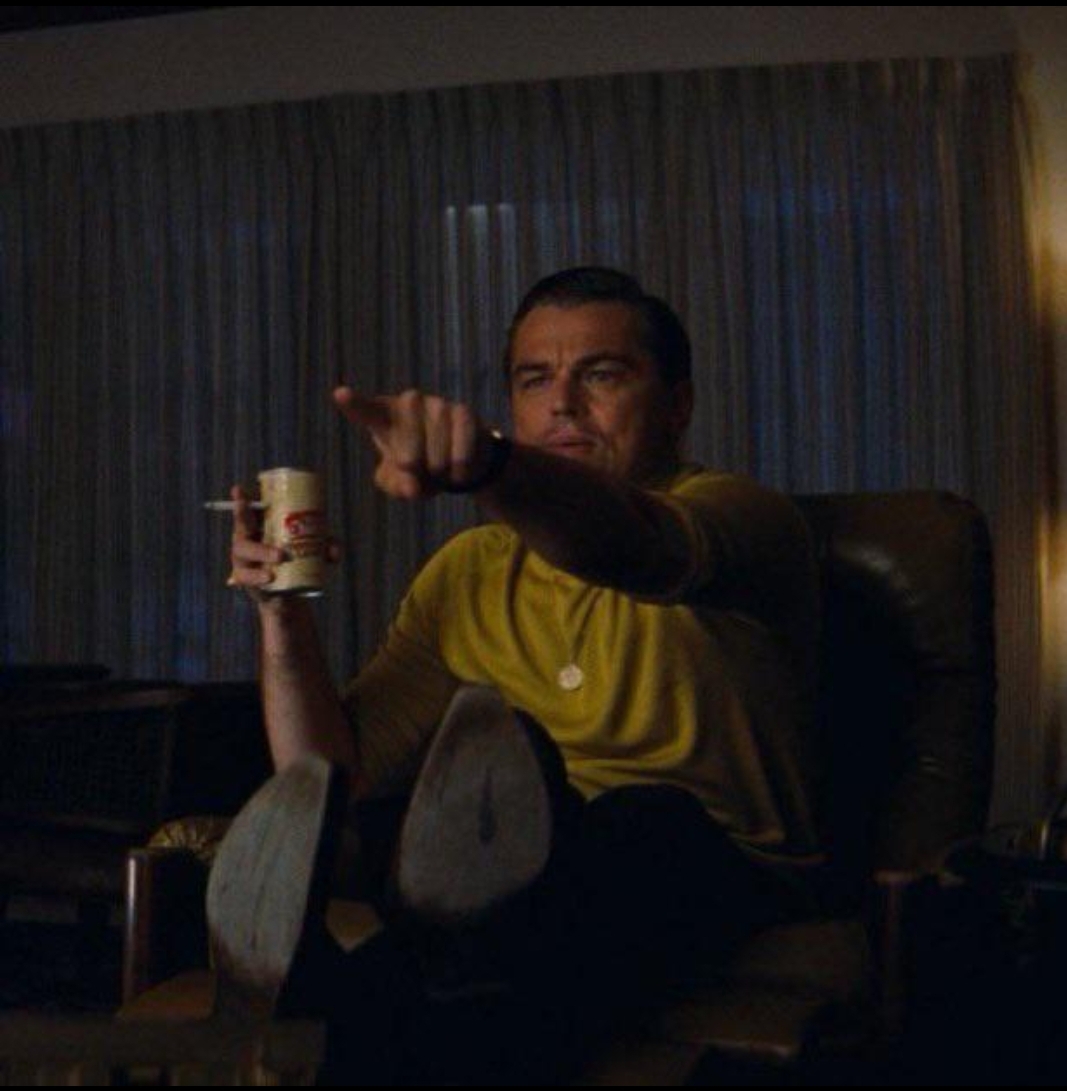 Leonardo DiCaprio Pointing meme template - Leonardo DiCaprio sits on a couch in a Hawaiian shirt, beer in hand, leaning forward and jabbing his finger at the television